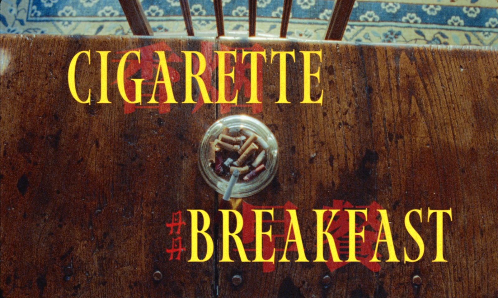 cigarette breakfast title frame: yellow serif titles over a wooden table with an ashtray of cigarette butts